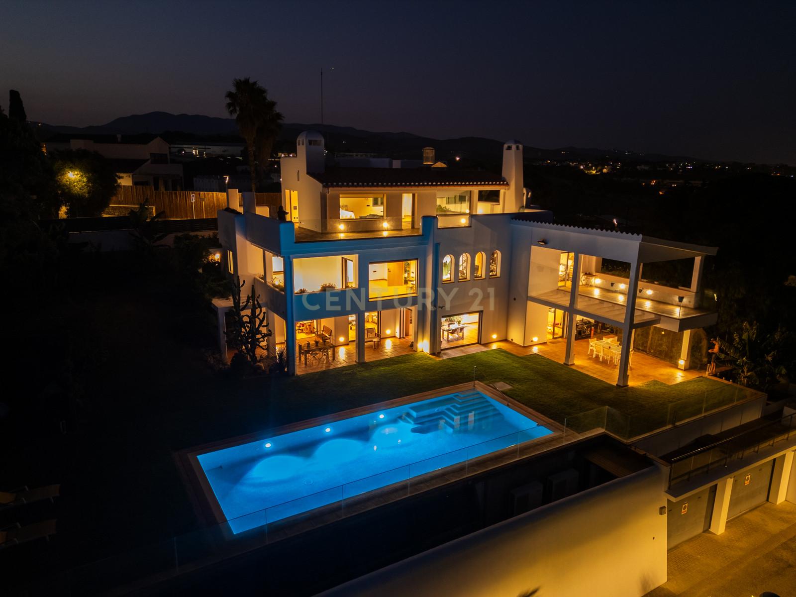 Villa Can Bonita illuminated at blue hour, infinity pool reflecting warm interior light above the Mediterranean coastline.