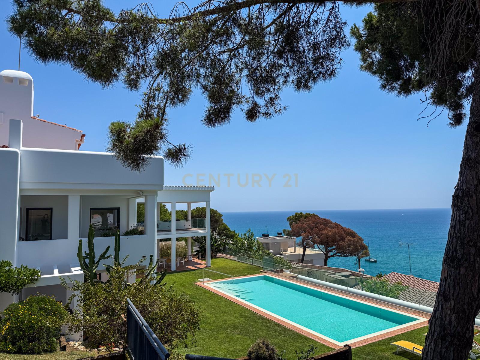 Aerial view of Villa Can Bonita's contemporary white architecture set on a terraced Mediterranean cliff above the sea.