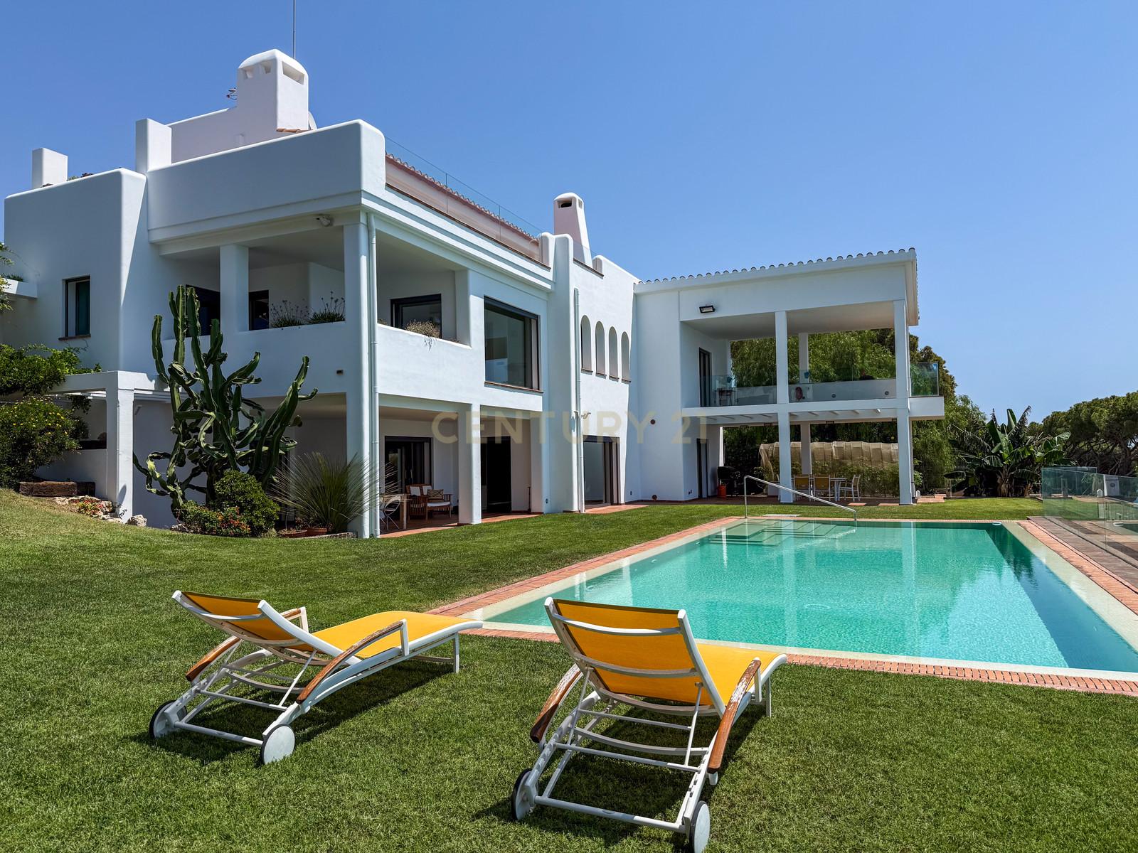 South-facing façade of Villa Can Bonita with deep loggias, lawn and infinity pool above the Mediterranean.